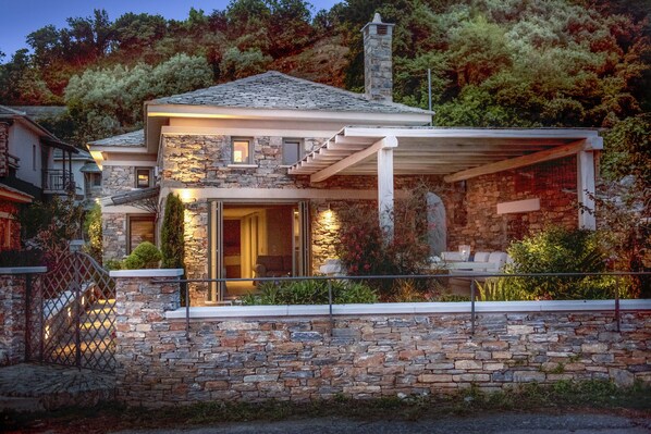Une maison en pierre dotée d’un porche couvert, d’une cheminée en pierre et d’un escalier menant à l’entrée.