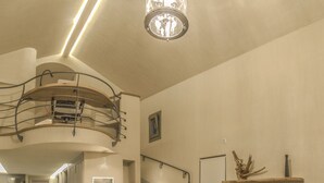 Ein geräumiger Wohnbereich mit hohen Decken, einer Holztreppe, einem großen Sofa, einem Holztisch und einem Flachbildfernseher auf einem Holzständer.