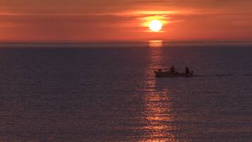 A sunset over a calm sea with a boat carrying people.