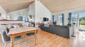 Ein großzügiger Wohnbereich mit Holztisch, grauem Sofa und Fernseher im Hintergrund.