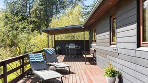 Eine überdachte Terrasse im Freien mit Liegestühlen, einem Tisch und einem Grill.