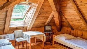 Een gezellig slaapkamer op zolder met een houten schuine dak, een kleine tafel met stoel, een enkel bed en een televisie op een standaard.