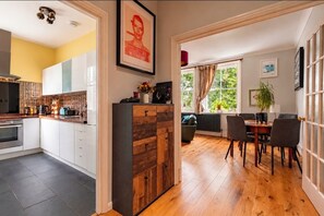 A modern kitchen with white cabinets, a wooden cabinet, and a dining area with a table and chairs. - Beautiful Highgate 2-Bed Apartment | Sunny Roof Terrace (London)