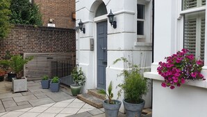 A courtyard with potted plants, a brick wall, and a white building with a blue door.