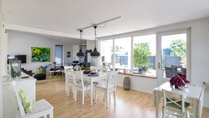 A spacious kitchen with white cabinetry, a dining area with white chairs, and large windows offering a view of the backyard. - Lovely home in Juelsminde with kitchen (Juelsminde)