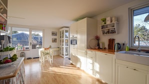 A bright kitchen with wooden flooring, white cabinets, and a window overlooking a backyard. - Lovely home in Juelsminde with kitchen (Juelsminde)