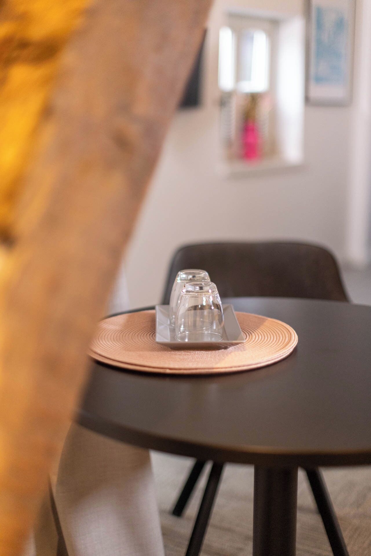 A dining table with a clear glass water glass and a square plate on a woven placemat.