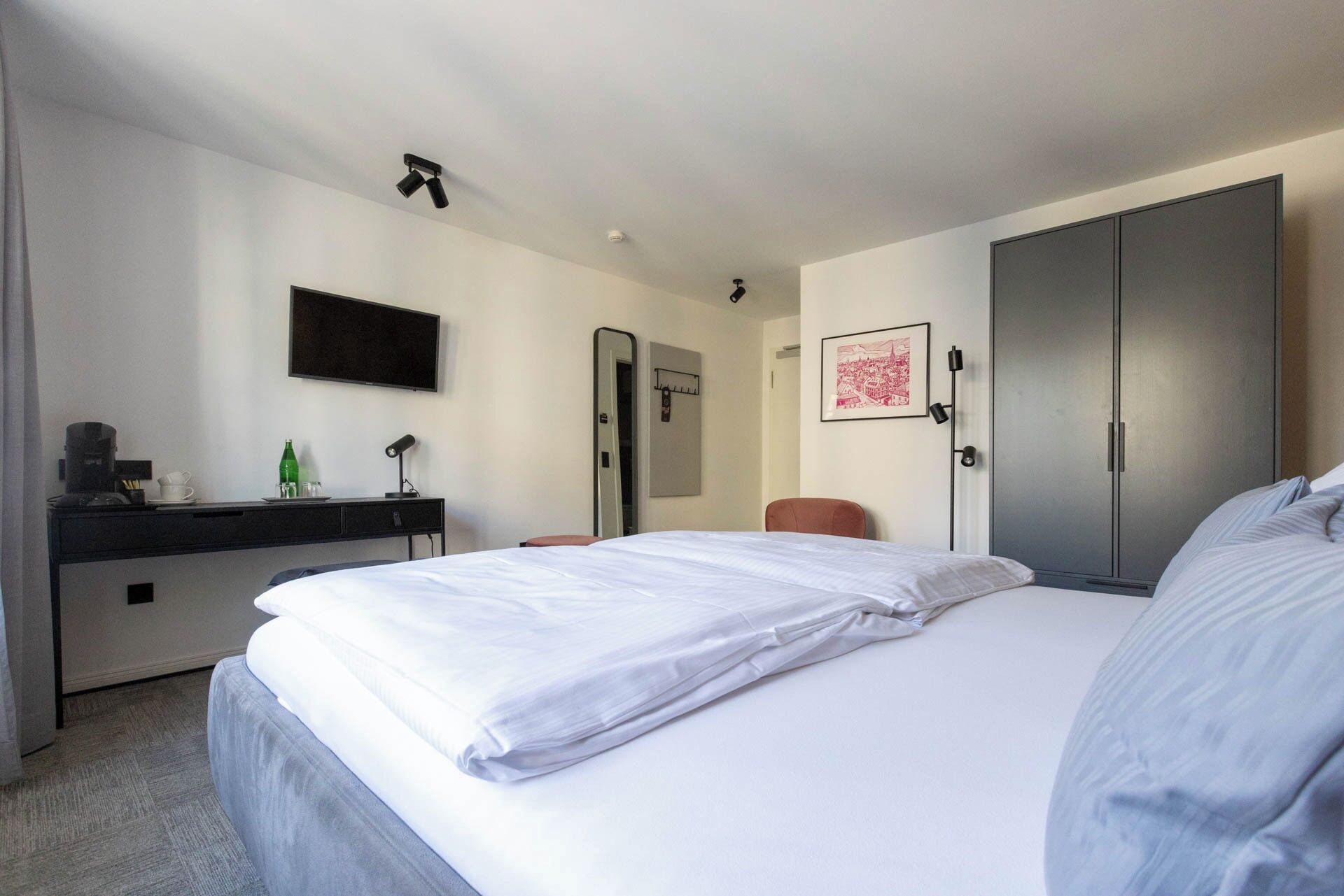 A hotel room with a large bed, a desk with a coffee maker, a flat-screen TV, and a wardrobe.