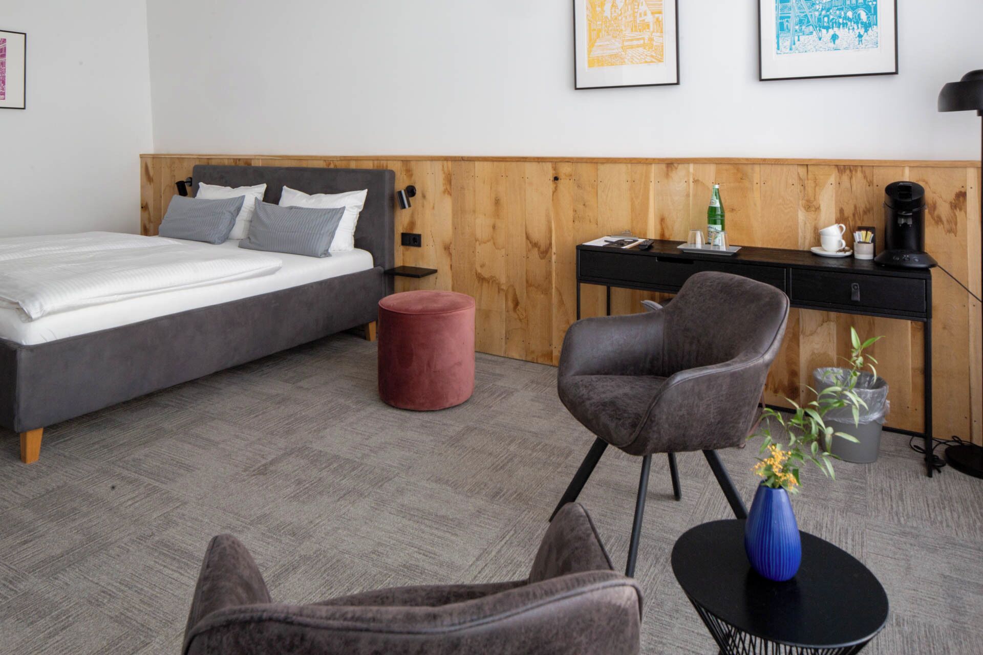 Ein modernes Hotelzimmer mit einem Bett, einem Schreibtisch, einem Stuhl und einem kleinen runden Tisch mit einer Vase.