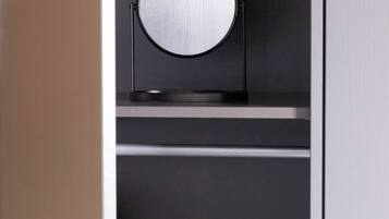 Une pièce moderne et minimaliste aux couleurs sombres, avec un grand miroir rond posé sur un support noir et une porte blanche.