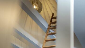 A wooden ladder in a room with a sloped ceiling and a hanging light fixture.