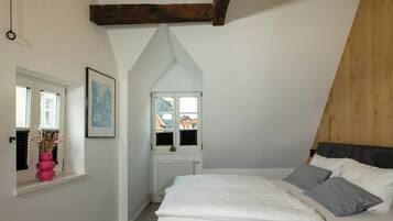 Un dormitorio con techo inclinado, una cama con almohadas, un radiador, una ventana con persianas y un cuadro enmarcado en la pared.