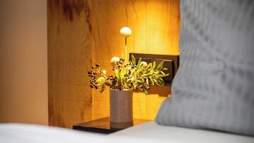 A neatly made bed with a white pillow, a bedside table with a lamp and a plant, and a wooden headboard with a wall-mounted light fixture.