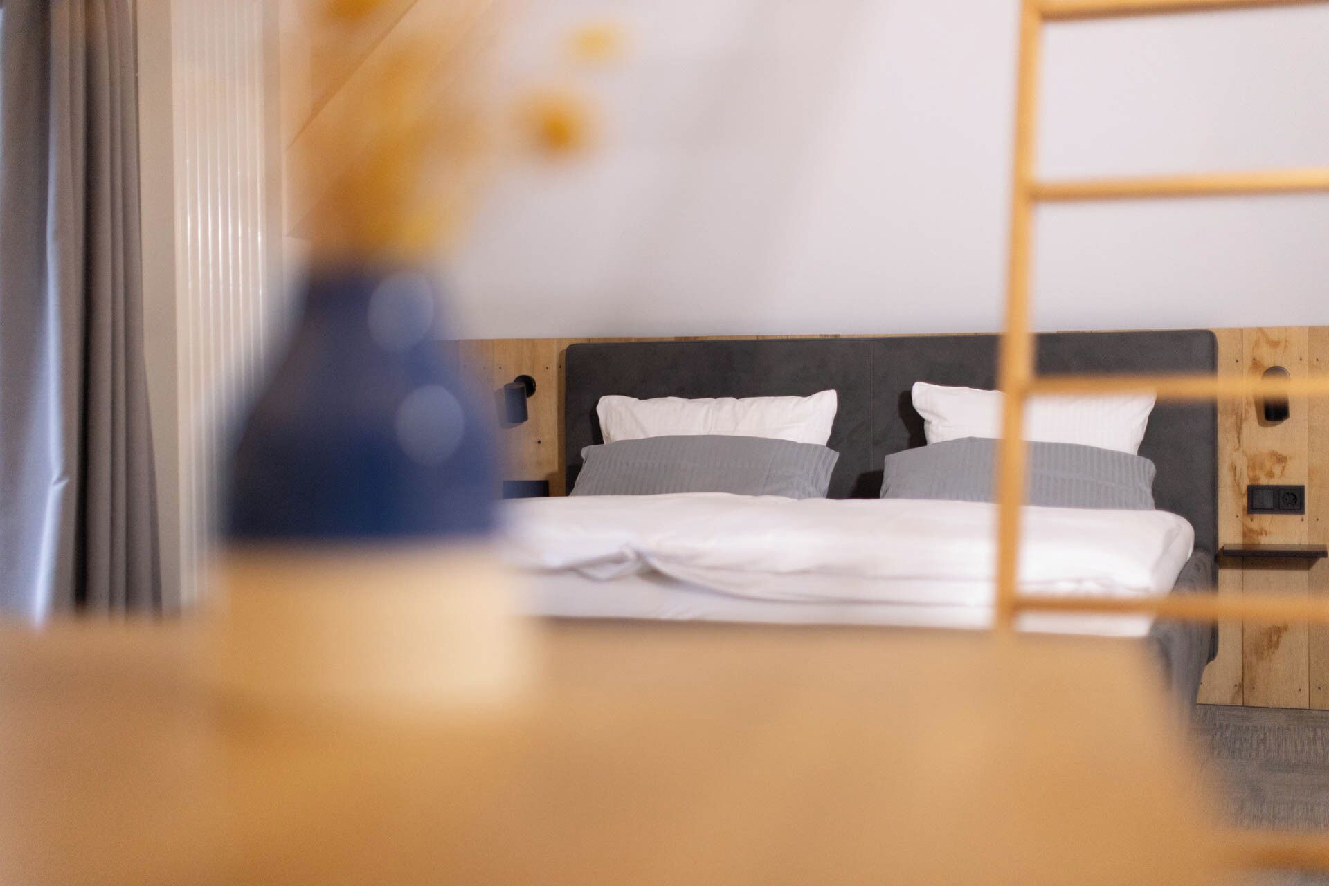 A neatly made bed with white and gray bedding, a wooden headboard, and a wooden nightstand with a lamp.