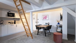 A modern kitchen with white cabinets, a microwave, and a coffee machine. There is a wooden ladder leaning against the ceiling, a dining area with black chairs, and a red ottoman. - Wertschätzer Hotel - Krumme Str. (Detmold)