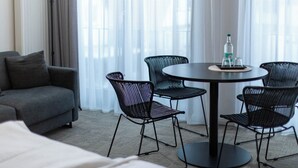 A hotel room with a grey sofa, a round table with four black chairs, and a bottle of water on the table. - Wertschätzer Hotel - Krumme Str. (Detmold)