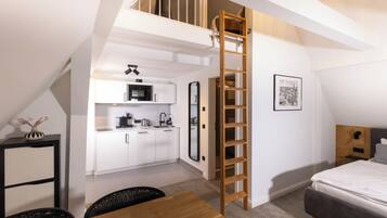 Un appartement compact et moderne doté d’une chambre en mezzanine, d’une kitchenette et d’une échelle en bois permettant d’accéder à l’espace de couchage supérieur.