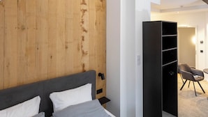 A bedroom with a wooden headboard, a bed with white and gray bedding, a black wardrobe, and a chair in a hallway. - Wertschätzer Hotel - Krumme Str. (Detmold)