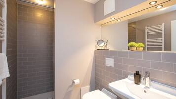 A modern bathroom with a shower, toilet, and sink, featuring grey tiles and a mirror with a towel rack.