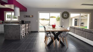 Uma cozinha moderna com uma ilha central, uma área de refeições com mesa e cadeiras de madeira, e uma grande janela com vista para uma piscina.