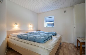 Et soveværelse med en seng, to væglamper, et vindue med persienner, et klædeskab og en lille træstol.