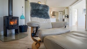 Ein modernes Wohnzimmer mit Kaminofen, einer gemütlichen Couch und einer Küche im Hintergrund.