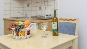 A kitchen with a table, a basket of fruit, a wine bottle, and a chair. - Welcome (Naxos)