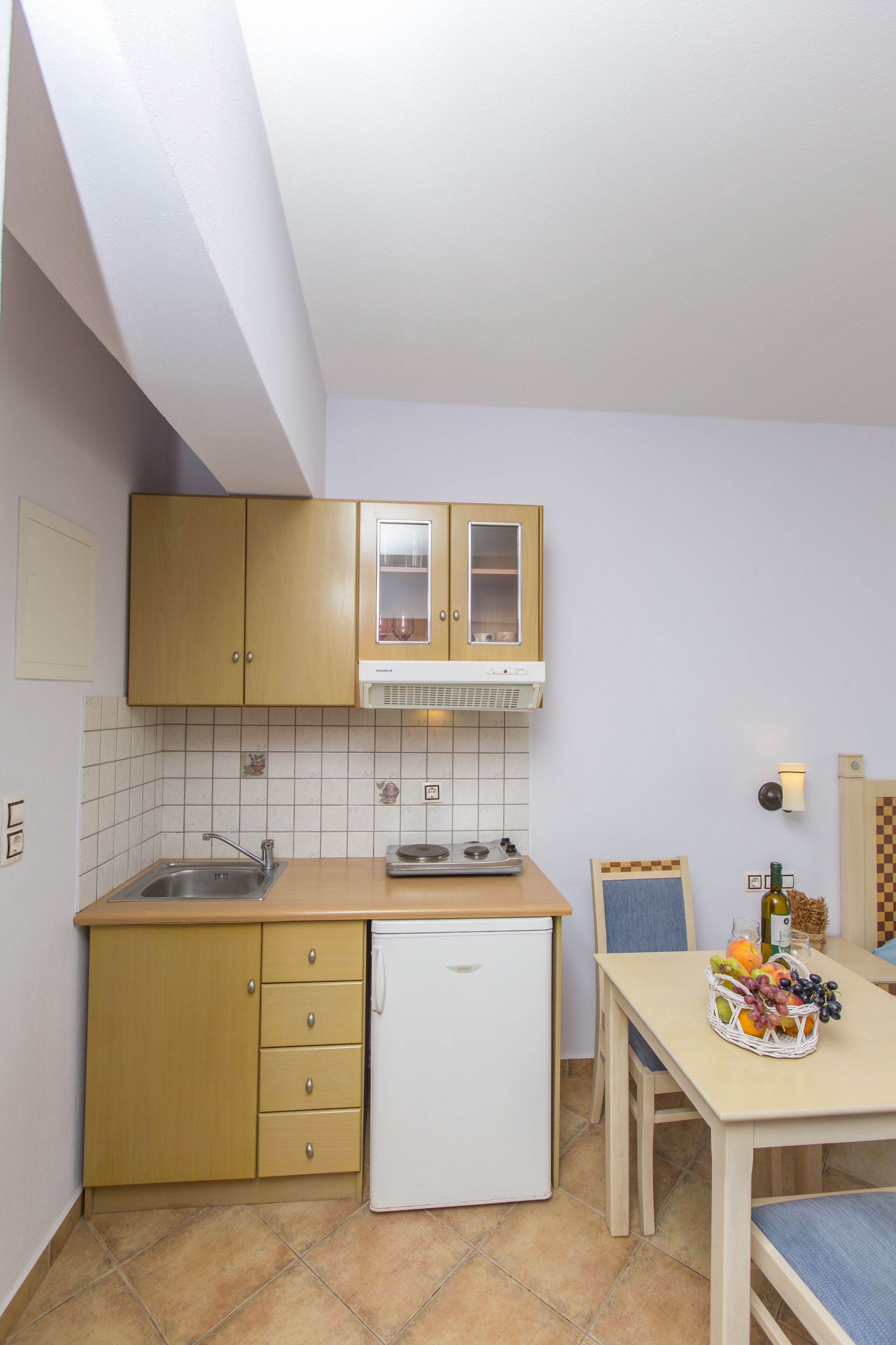 A compact kitchen with wooden cabinets, a white refrigerator, and a tiled backsplash.