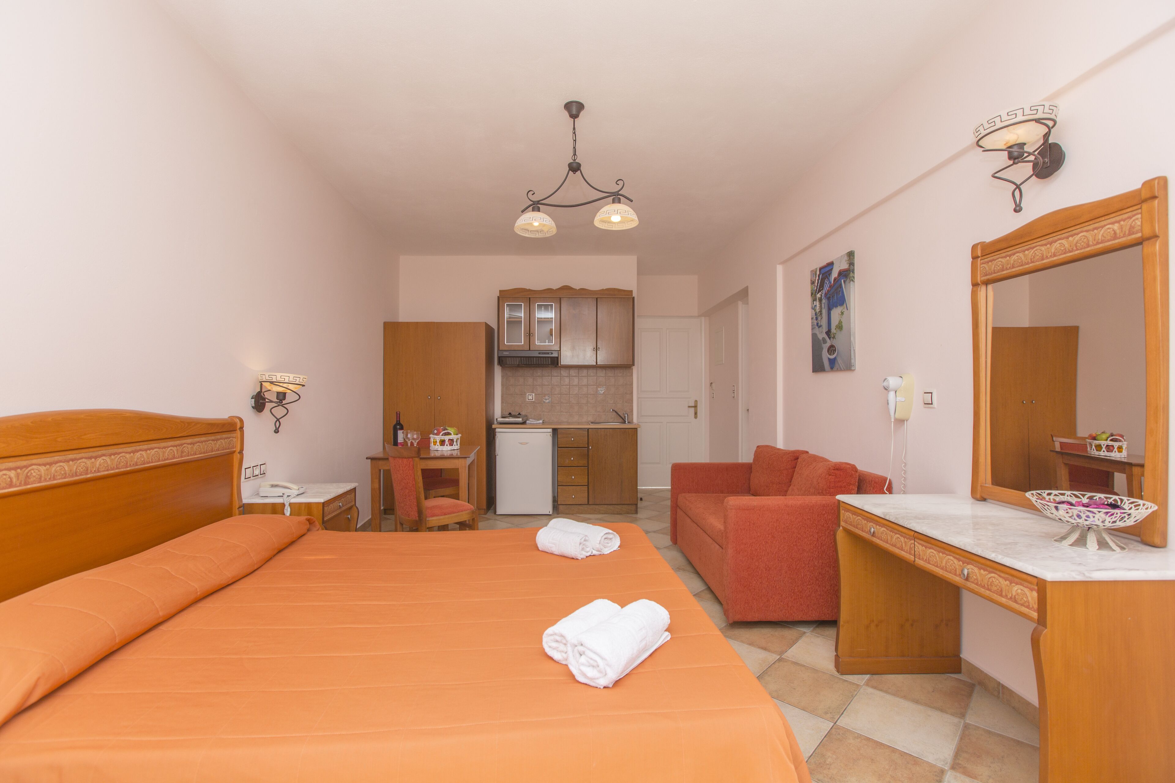 A hotel room with a bed, a desk, a chair, a sofa, a kitchen area, and a bathroom.