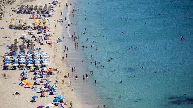 A beach with rows of umbrellas and people swimming and sunbathing. - Welcome (Naxos)