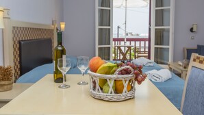 A hotel room with a bed, a table with a bottle of wine, glasses, and a fruit basket. - Welcome (Naxos)