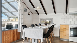 Zona pranzo con tavolo imbandito per quattro persone, sedie in legno, lampada a sospensione moderna e cucina con piano cottura e mobili.