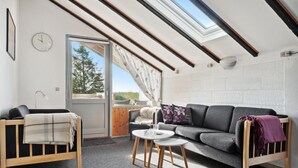 Una stanza accogliente con soffitto spiovente, un divano, un tavolino e una finestra vista alberi.