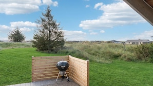 Un patio con una griglia barbecue, una recinzione in legno e un'area verde con un albero e edifici in lontananza.