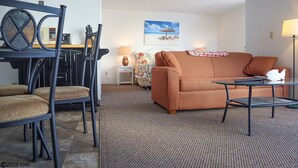 A living room with a sofa, chairs, a glass coffee table, a lamp, and a painting on the wall. - Pet Friendly Beachfront Vacation Condo At Bargain Price! (Fort Myers Beach)