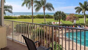 A balcony with a view of a pool, palm trees, and a beach. - Pet Friendly Beachfront Vacation Condo At Bargain Price! (Fort Myers Beach)