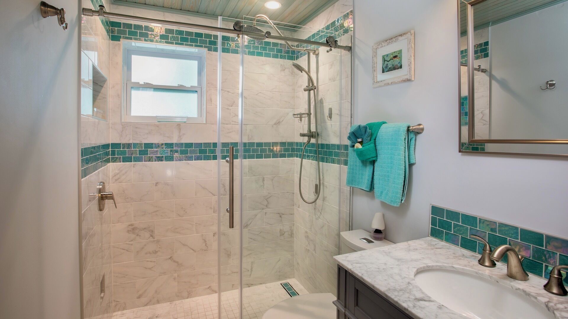 A bathroom with a glass-enclosed shower, a sink with a marble countertop, and a tiled backsplash.