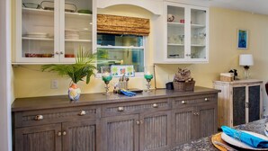 A kitchen with wooden cabinets, a window with a bamboo blind, and a countertop with a plant and cocktail glasses. - BAREFOOT BUNGALOW~2 Bedroom, 2 Bathroom Home w/ Office, Pool and Tiki Hut! (Key West)