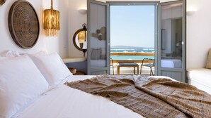 A bedroom with a large bed, a view of the sea, and a balcony with a table and chairs.