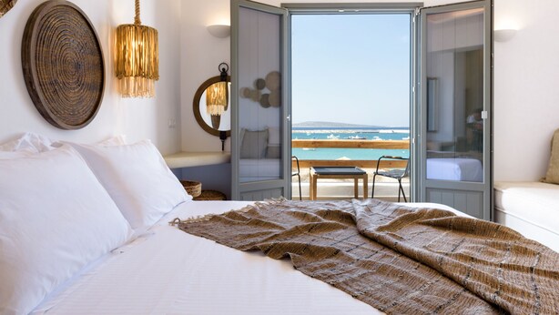 A bedroom with a large bed, a view of the sea, and a balcony with a table and chairs. - Kiano Suites Paros (Paros)