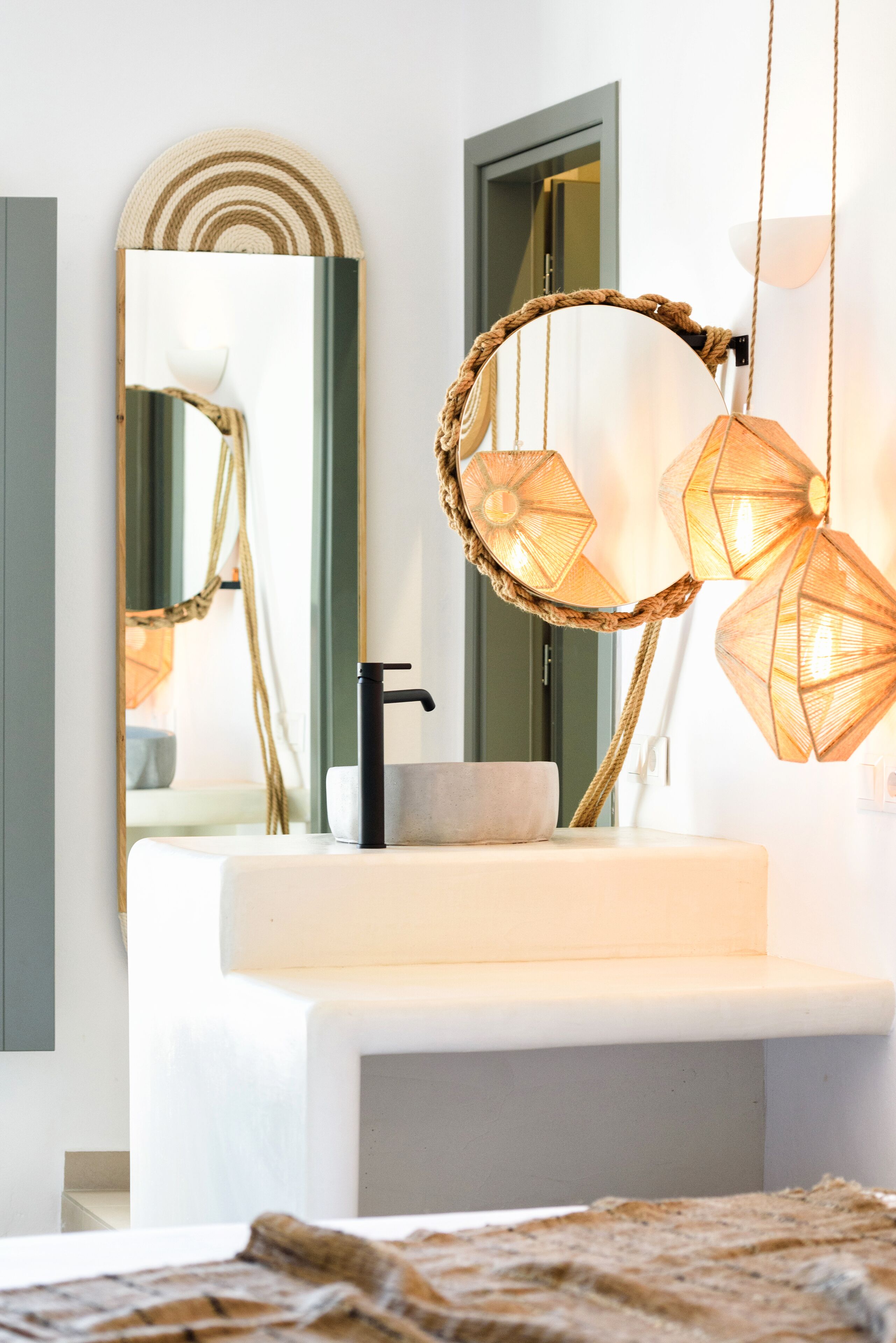 A modern bathroom with a white sink, a black faucet, and a mirror with a woven frame.