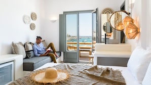 A modern hotel room with a balcony, a sofa, a reading area, and decorative wall art. - Kiano Suites Paros (Paros)
