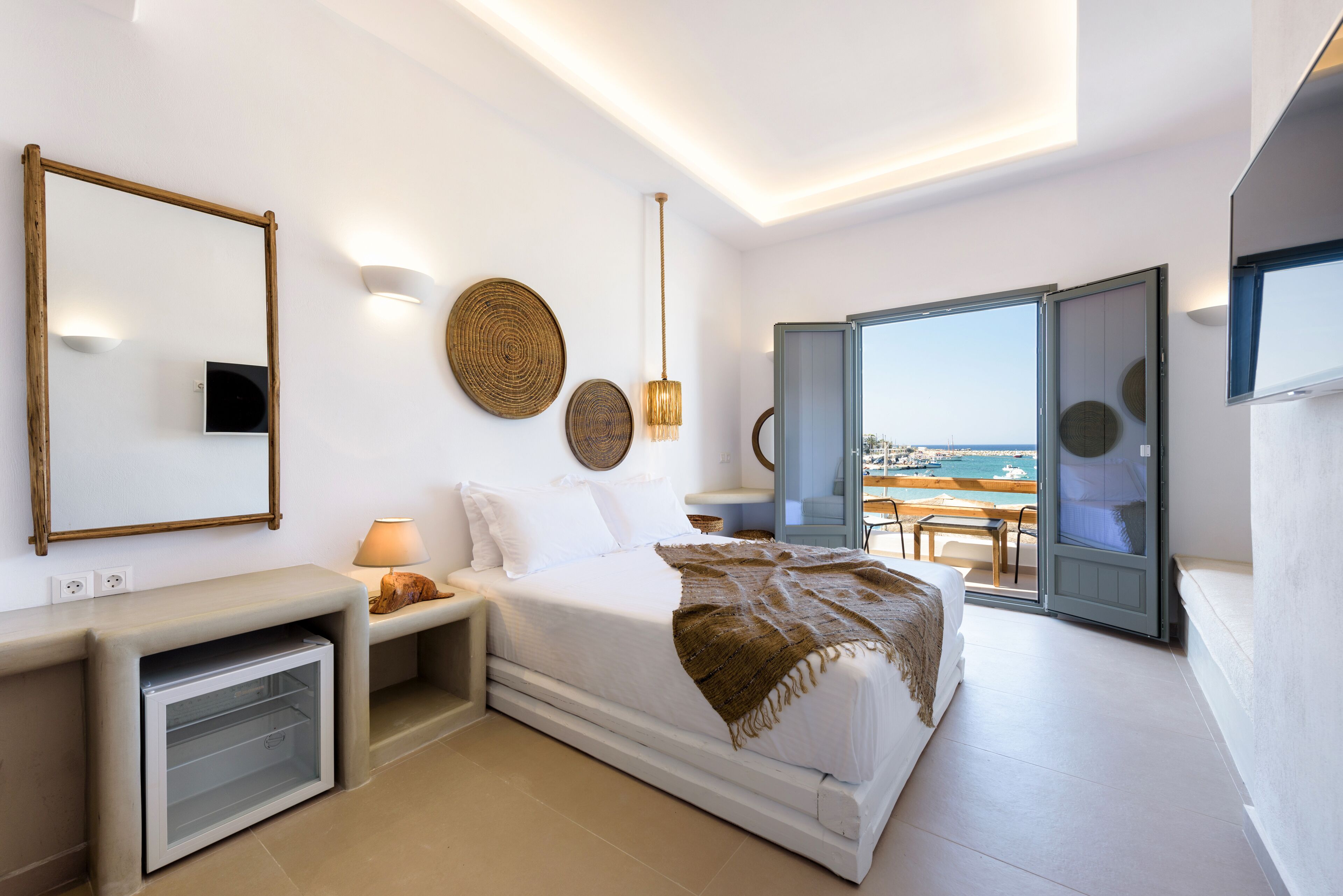 A modern bedroom with a bed, bedside table, lamp, and a view of the sea through a sliding door.