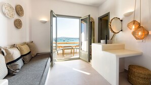 A room with a sofa, a small table, a mirror, and a view of the beach. - Kiano Suites Paros (Paros)