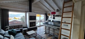 Un interior moderno con chimenea, barra de cocina y grandes ventanales con vistas panorámicas.