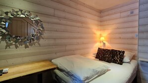 Een gezellige kamer met een houten plafond, een bed met wit beddengoed, een decoratieve spiegel en een wandlamp.