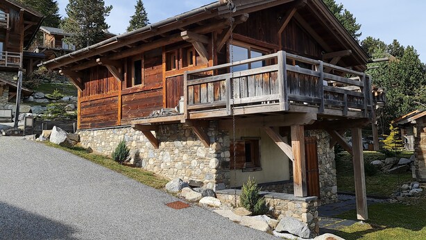 Een houten chalet met balkon, stenen fundering en een stenen muur.