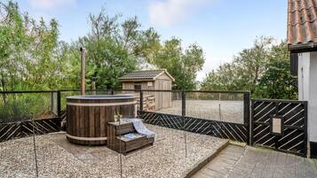 Un bain à remous en bois, doté d’un banc, entouré d’une zone recouverte de gravier et délimité par une clôture en métal.
