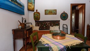Un comedor con una mesa de madera, sillas y un mantel colorido. Hay un cuadro en la pared y un cabecero decorativo detrás de la mesa.
