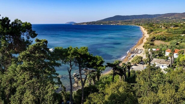 Un paisaje costero con playa, mar azul cristalino y montañas al fondo.